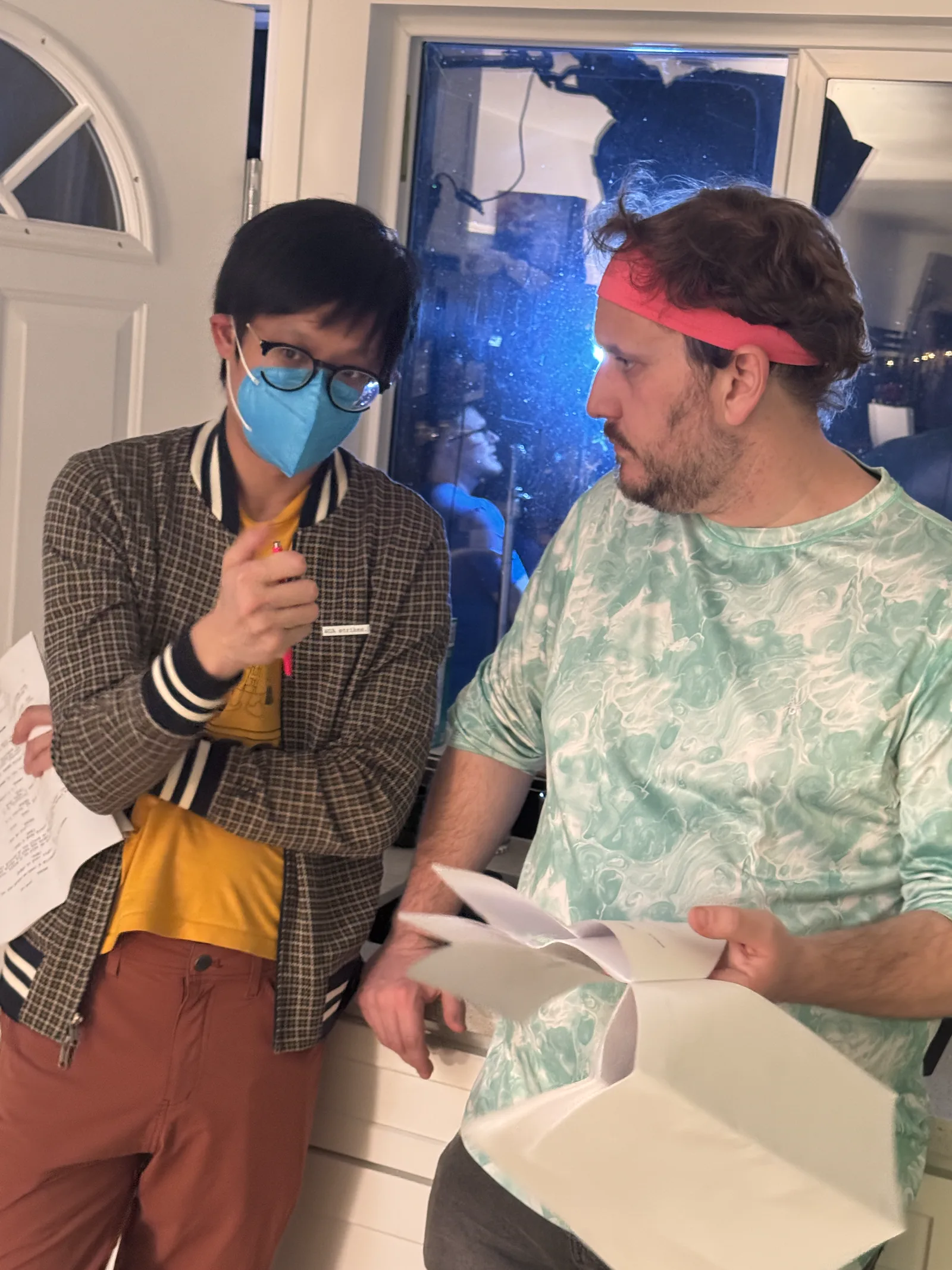 Two masked crew members looking over pages on set