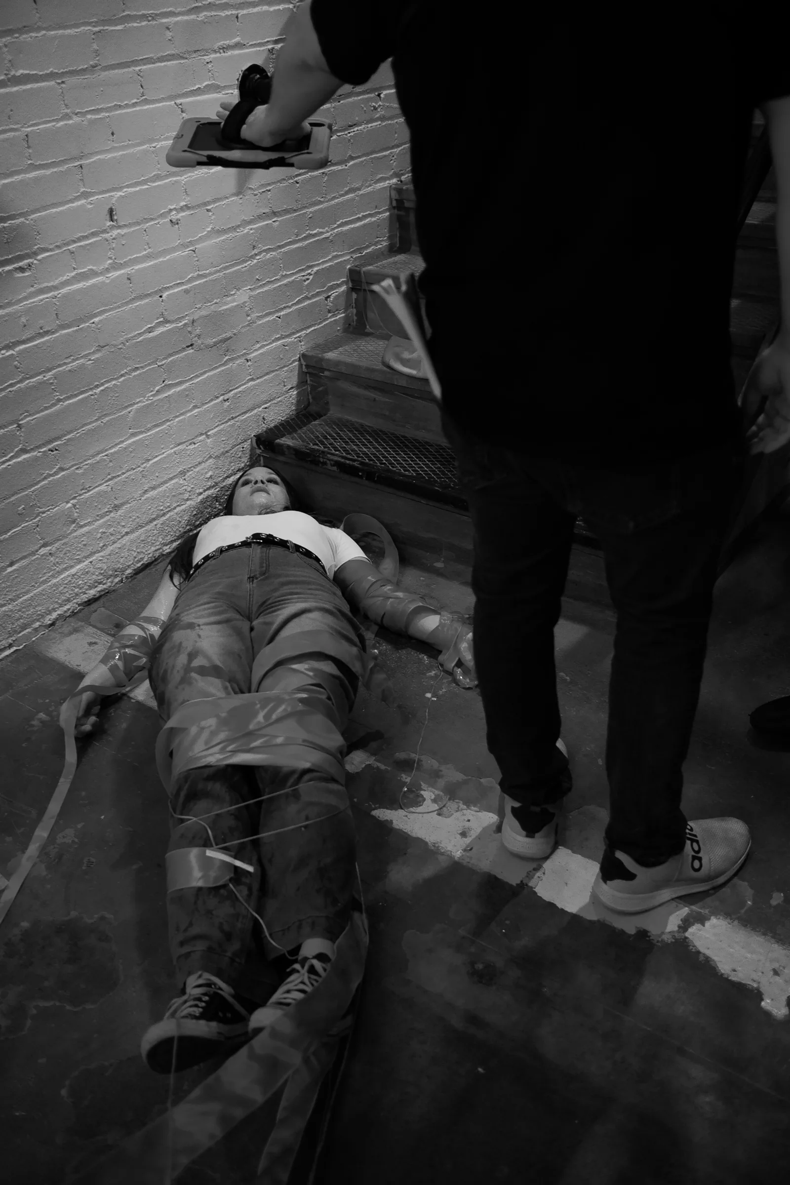 Black and white photo of an actor lying on a concrete floor during a stunt rehearsal